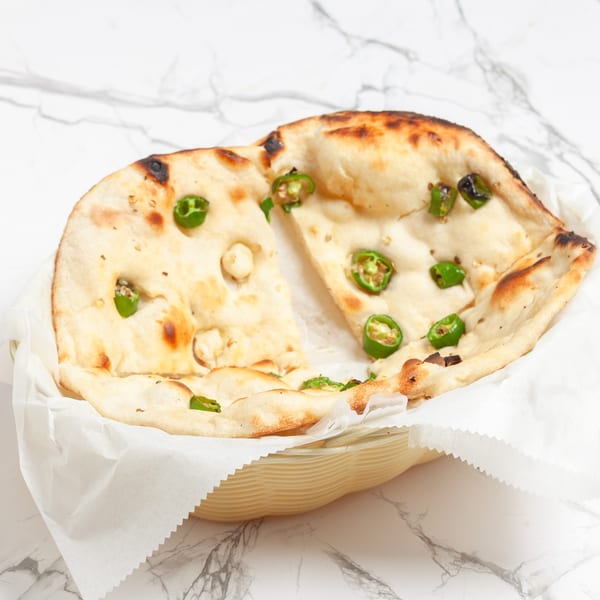 Indian naan bread with green chili slices, served in a basket with white paper lining.