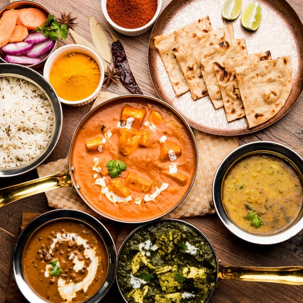 An overhead view of various Indian dishes including paneer, dal, rice, naan, and spices on a wooden table.