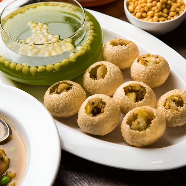 Indian Pani Puri, a popular street food, with a bowl of green spiced water and a side of boondi.