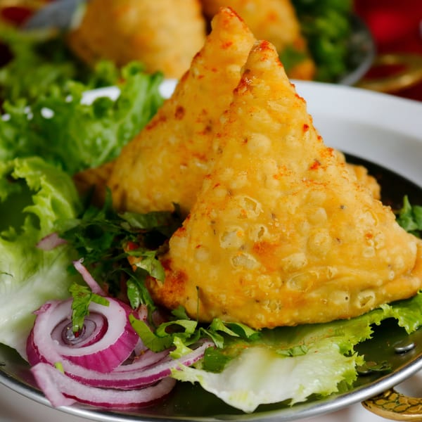 Two golden-brown Indian samosas, sprinkled with spices, served on a bed of fresh lettuce and red onion.