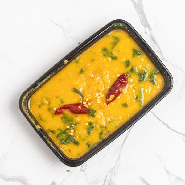 Indian dal in a black container, garnished with red chilies and green herbs, on a marble surface.
