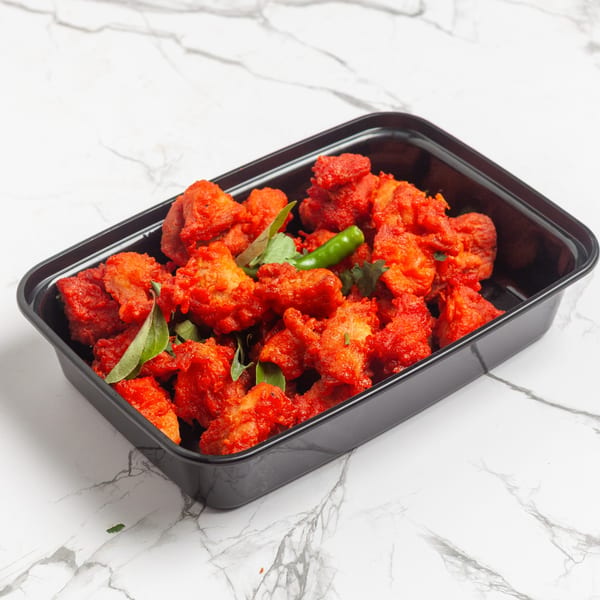 Bright red Indian 5 Stars Restaurant chicken tikka pieces with green chilies and herbs in a black container.
