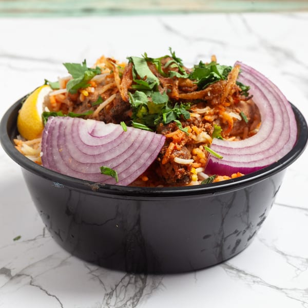 Indian biryani in a black bowl, garnished with red onion, lemon, and fresh cilantro.