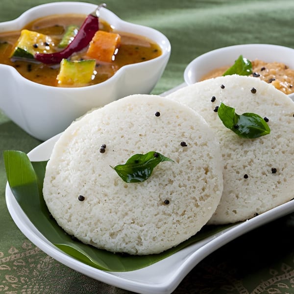 Indian idli with sambar and chutney, garnished with curry leaves and mustard seeds.