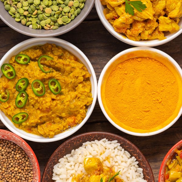 Overhead view of various Indian dishes and spices, including dal, chicken curry, rice, and turmeric.