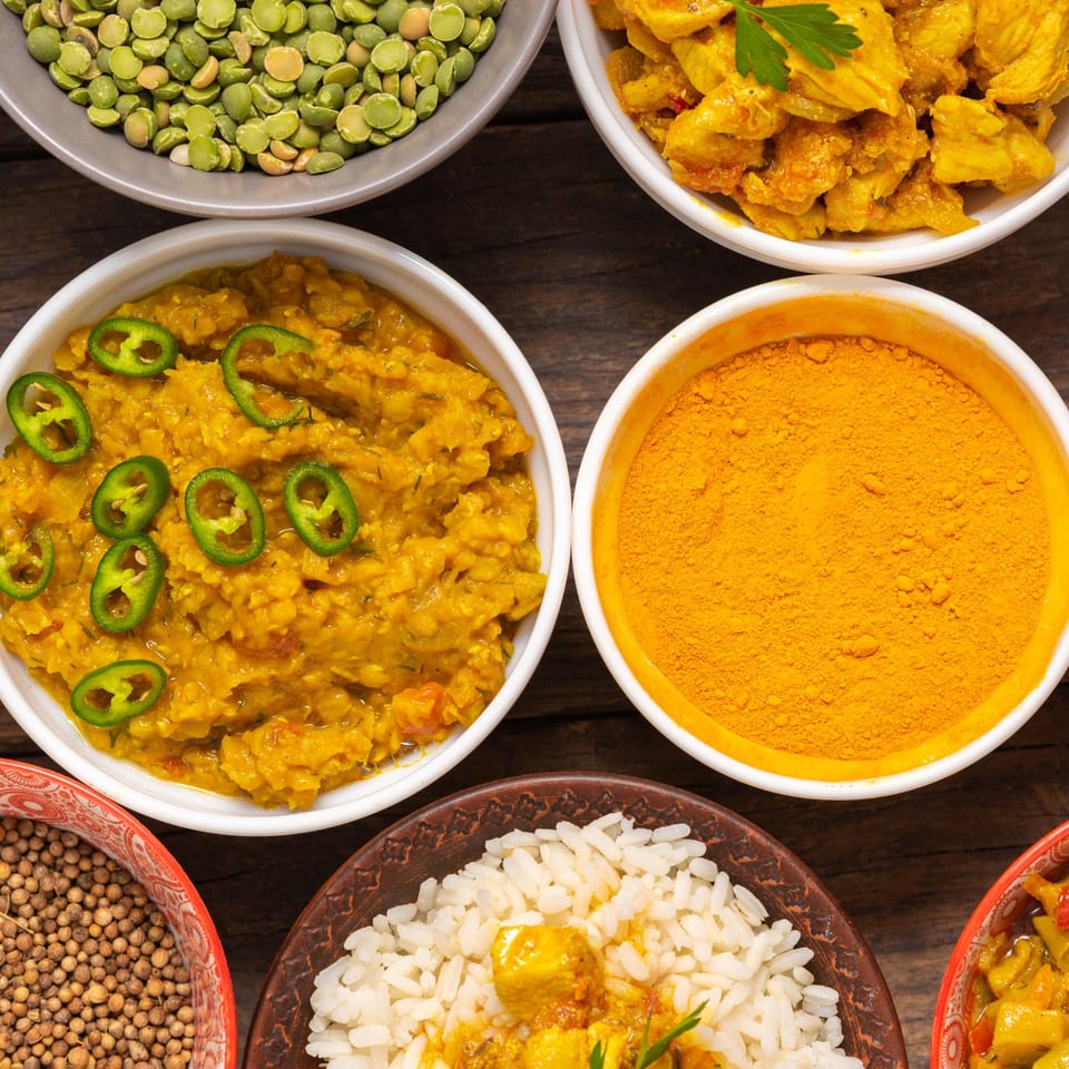 Overhead view of various Indian dishes and spices, including dal, chicken curry, rice, and turmeric.